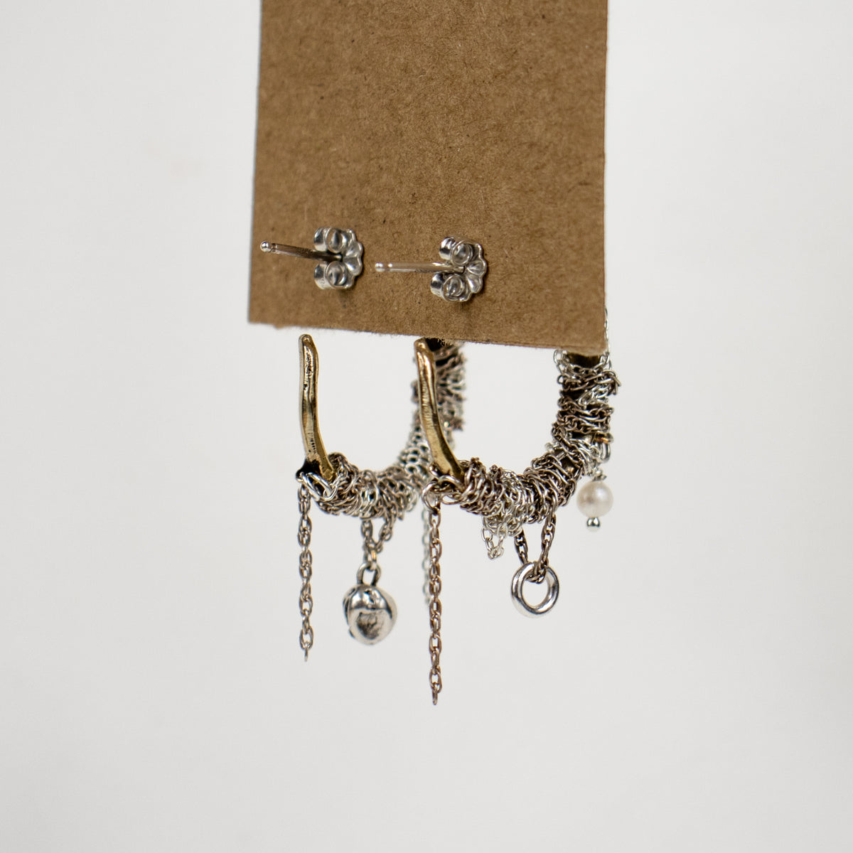 Brass hoop earrings wrapped with sterling silver chain beaded with a pearl, silver seaweed charm, jump-ring, and tassels and finished with sterling silver posts and backings handmade and finished in our Catskills store-studio by Kria World shown on kraft paper tag on white background.