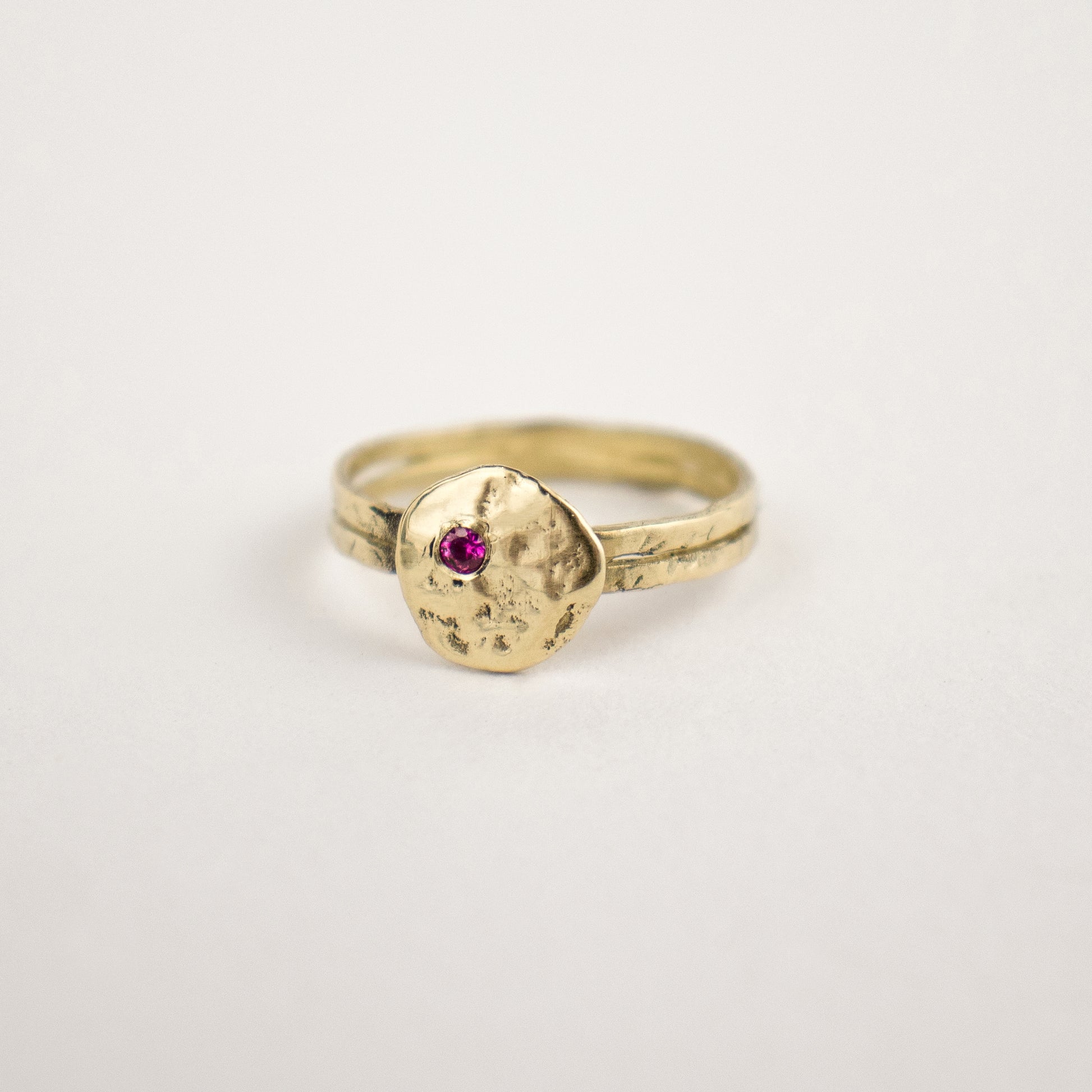 Hammer-finished solid reclaimed 14k gold Maine rock 0.5 inch in diameter set with one 2mm pink sapphire.  Made-to-order and finished in our Catskills store-studio.