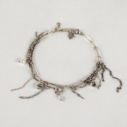 A layered silver-tone chain bracelet by Kria World with multiple dangling charms, including small cast seaweed charms, pearl beads, and a clear faceted bead, displayed on a white background.