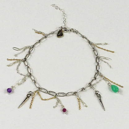 A silver chain bracelet handmade by Kria World with multiple dangling charms, including spikes, chains, and small beads in purple, green, and magenta, displayed on a light gray background.
