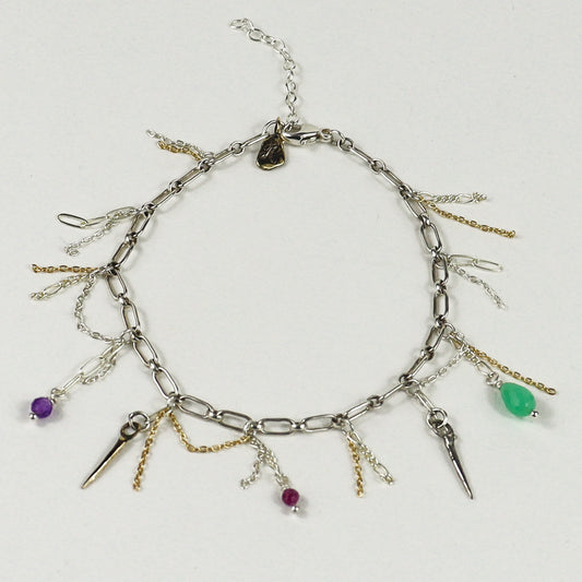 A silver chain bracelet handmade by Kria World with multiple dangling charms, including spikes, chains, and small beads in purple, green, and magenta, displayed on a light gray background.