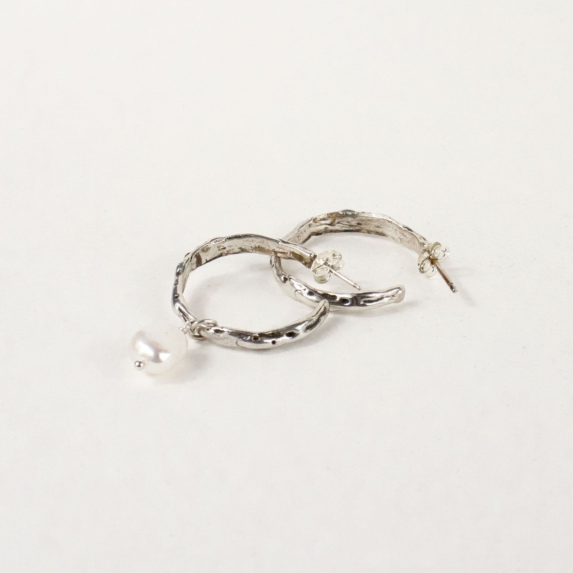 Sterling silver melted hoop earrings available in 1 inch and 0.5 inch diameters with one freshwater pearl handmade and finished in our Catskills store-studio