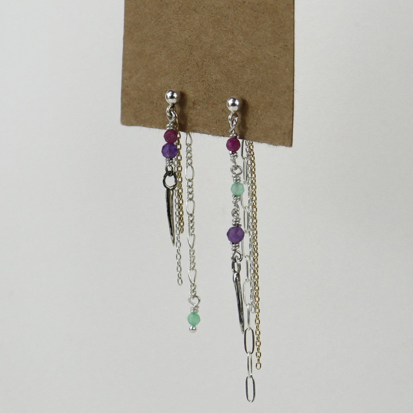 Sterling silver and gold-filled double mixed-chain tassels 2 inches at their longest dangling from sterling studs hand-beaded with ruby, amethyst, and chrysoprase and finished with tiny sterling and brass spikes hanging from paper tag on white background.