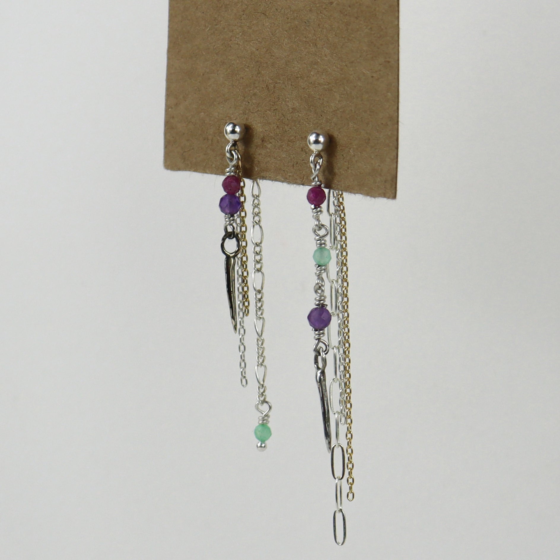 Sterling silver and gold-filled double mixed-chain tassels 2 inches at their longest dangling from sterling studs hand-beaded with ruby, amethyst, and chrysoprase and finished with tiny sterling and brass spikes hanging from paper tag on white background.