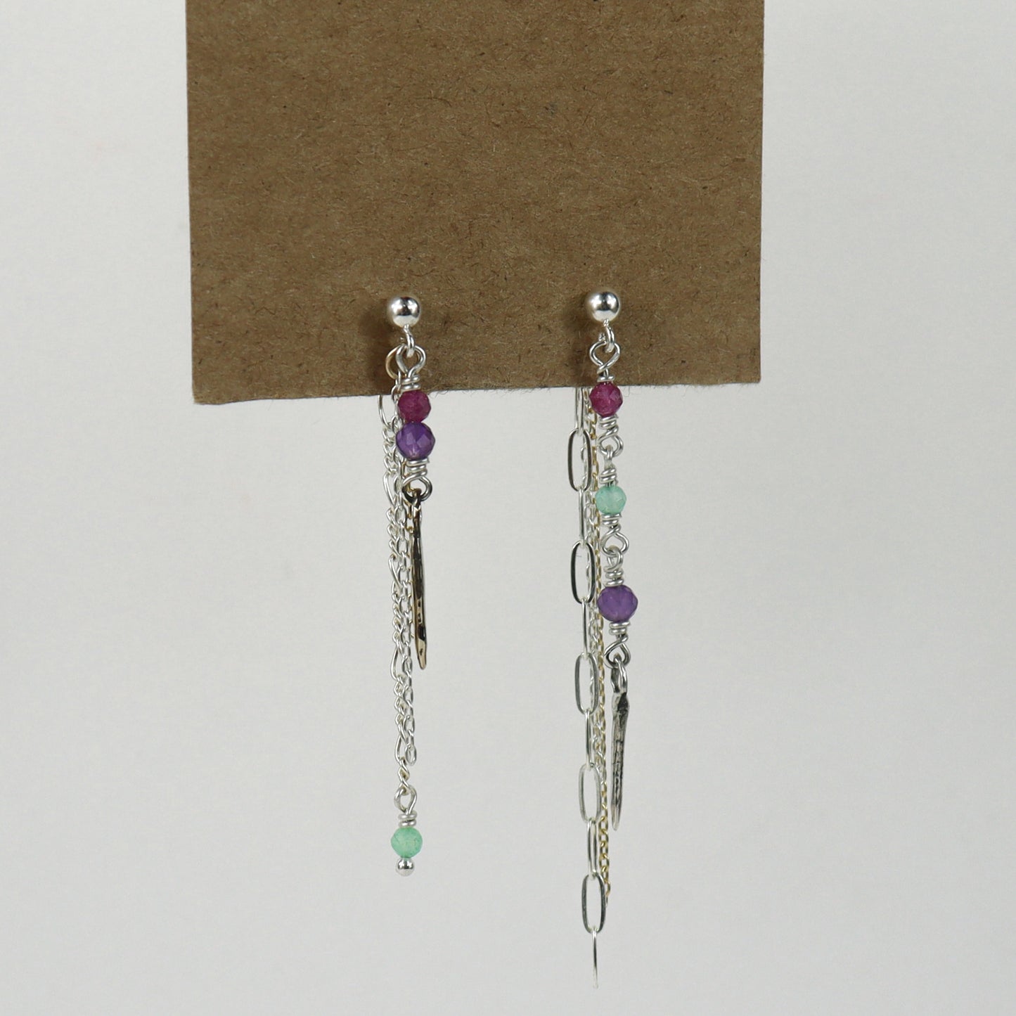 Sterling silver and gold-filled double mixed-chain tassels 2 inches at their longest dangling from sterling studs hand-beaded with ruby, amethyst, and chrysoprase and finished with tiny sterling and brass spikes hanging from paper tag on white background.