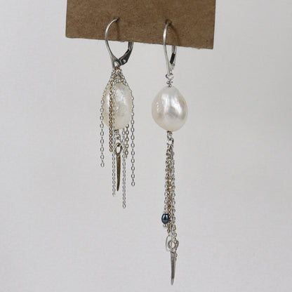 Asymmetrical sterling silver hoop earrings with two large freshwater pearls and one tiny black pearl with gold-filled and silver double mixed-chain tassels 2 and 3 inches each shown on paper tag on white background.