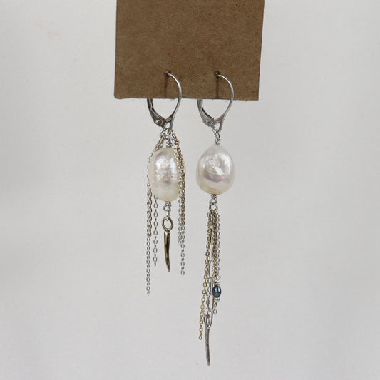 Asymmetrical sterling silver hoop earrings with two large freshwater pearls and one tiny black pearl with gold-filled and silver double mixed-chain tassels 2 and 3 inches each shown on paper tag on white background.