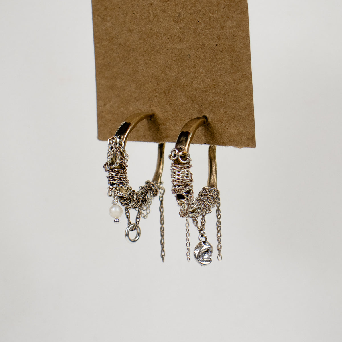Brass hoop earrings wrapped with sterling silver chain beaded with a pearl, silver seaweed charm, jump-ring, and tassels and finished with sterling silver posts and backings handmade and finished in our Catskills store-studio by Kria World shown on kraft paper tag on white background.