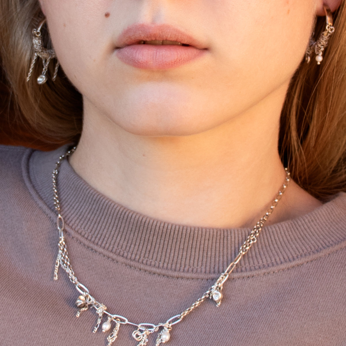 Brass hoop earrings wrapped with sterling silver chain and silver necklace beaded with pearl and tassels by Kria World shown on a model with blonde hair wearing a plum color sweatshirt.