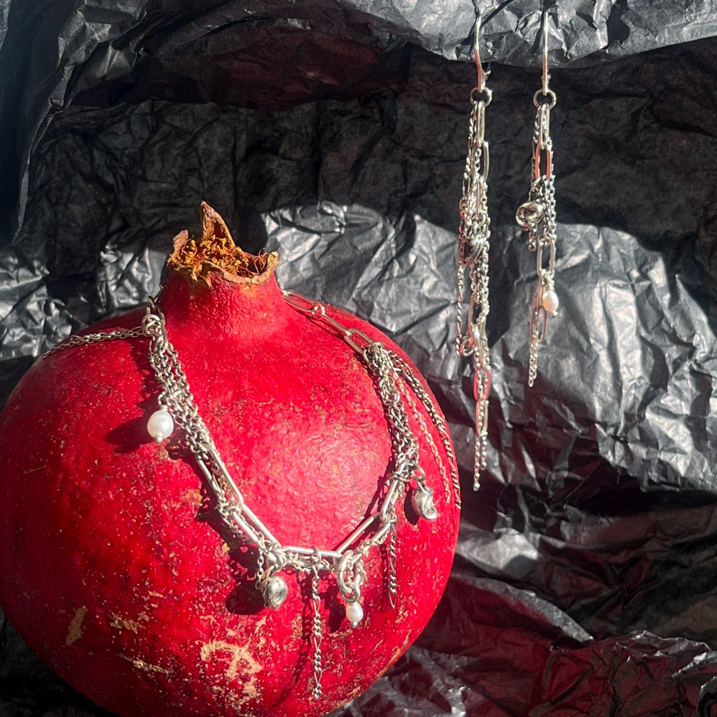 Two reclaimed sterling silver seaweed pods, tangled silver mixed-chain tassels, and freshwater pearl earrings and reclaimed sterling silver seaweed pods, tangled silver chain, and freshwater pearls on sterling mixed-chain necklace in still life with pomegranate.