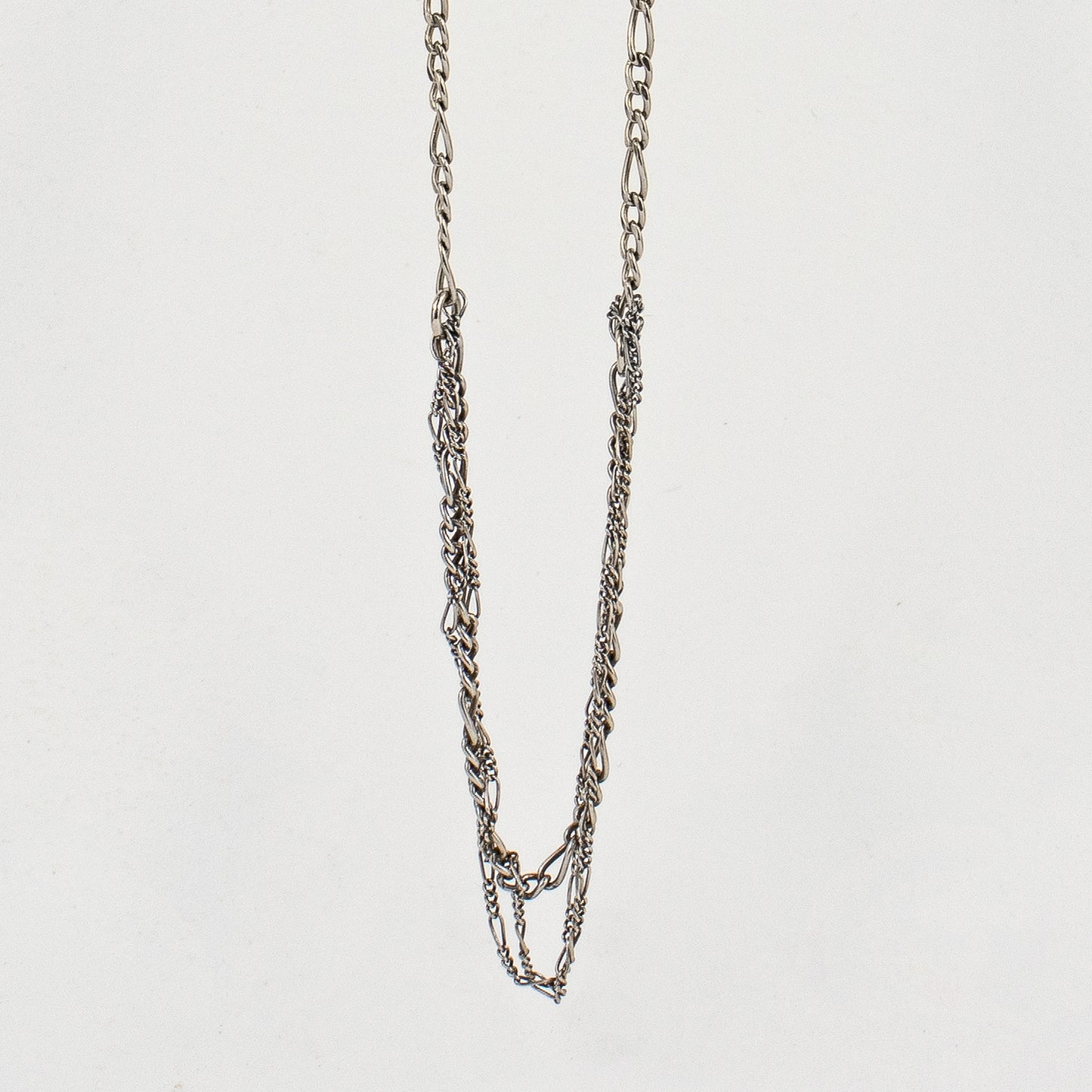 Tangled sterling silver mixed Figaro chains adjustable 20 - 22 inches shown hanging over off-white background by Kria Jewelry.