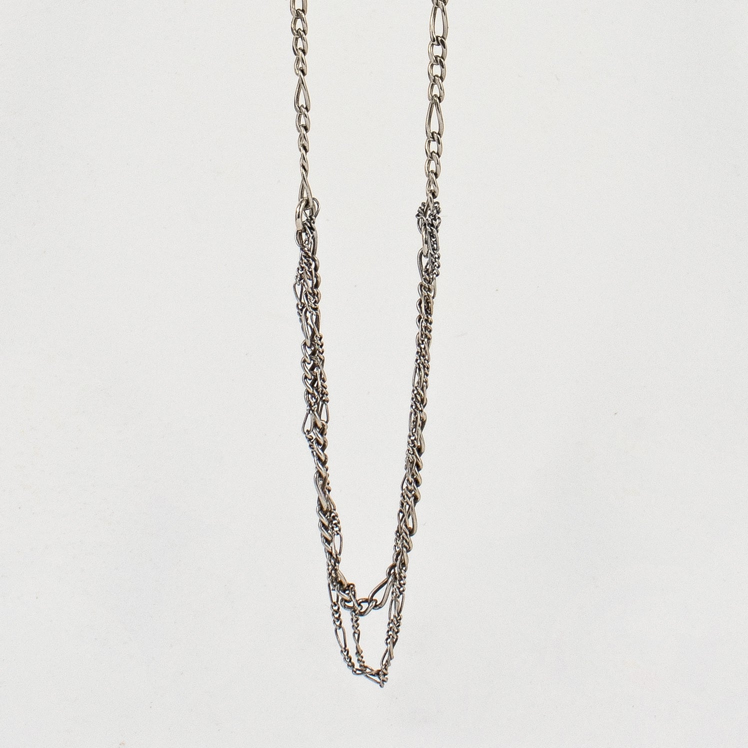 Tangled sterling silver mixed Figaro chains adjustable 20 - 22 inches shown hanging over off-white background by Kria Jewelry.