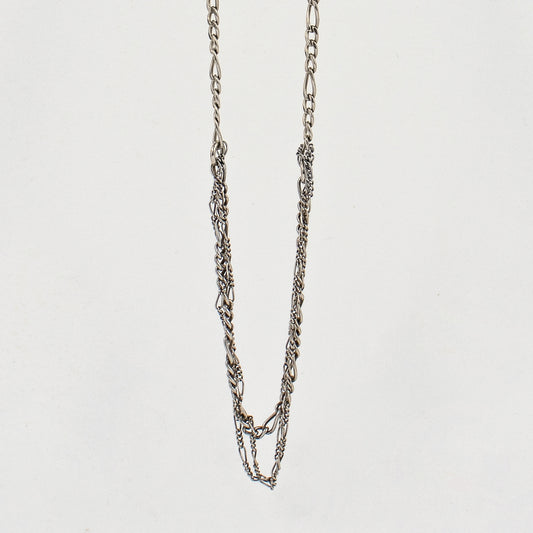 Tangled sterling silver mixed Figaro chains adjustable 20 - 22 inches shown hanging over off-white background by Kria Jewelry.