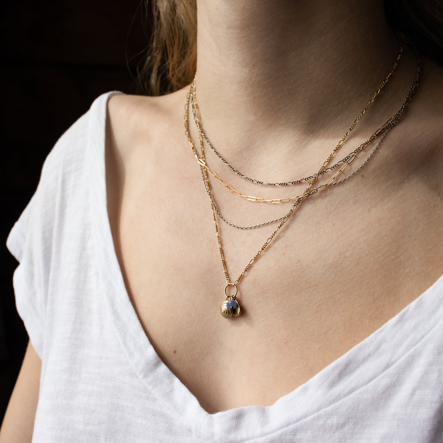 Solid reclaimed 10k gold spiral snail shell and rock disc charms with baby blue sapphire bead on gold-filled Figaro chain adjustable 18 -22 inches handmade and finished in our Catskills store-studio shown on model with fine mixed-chain necklace.