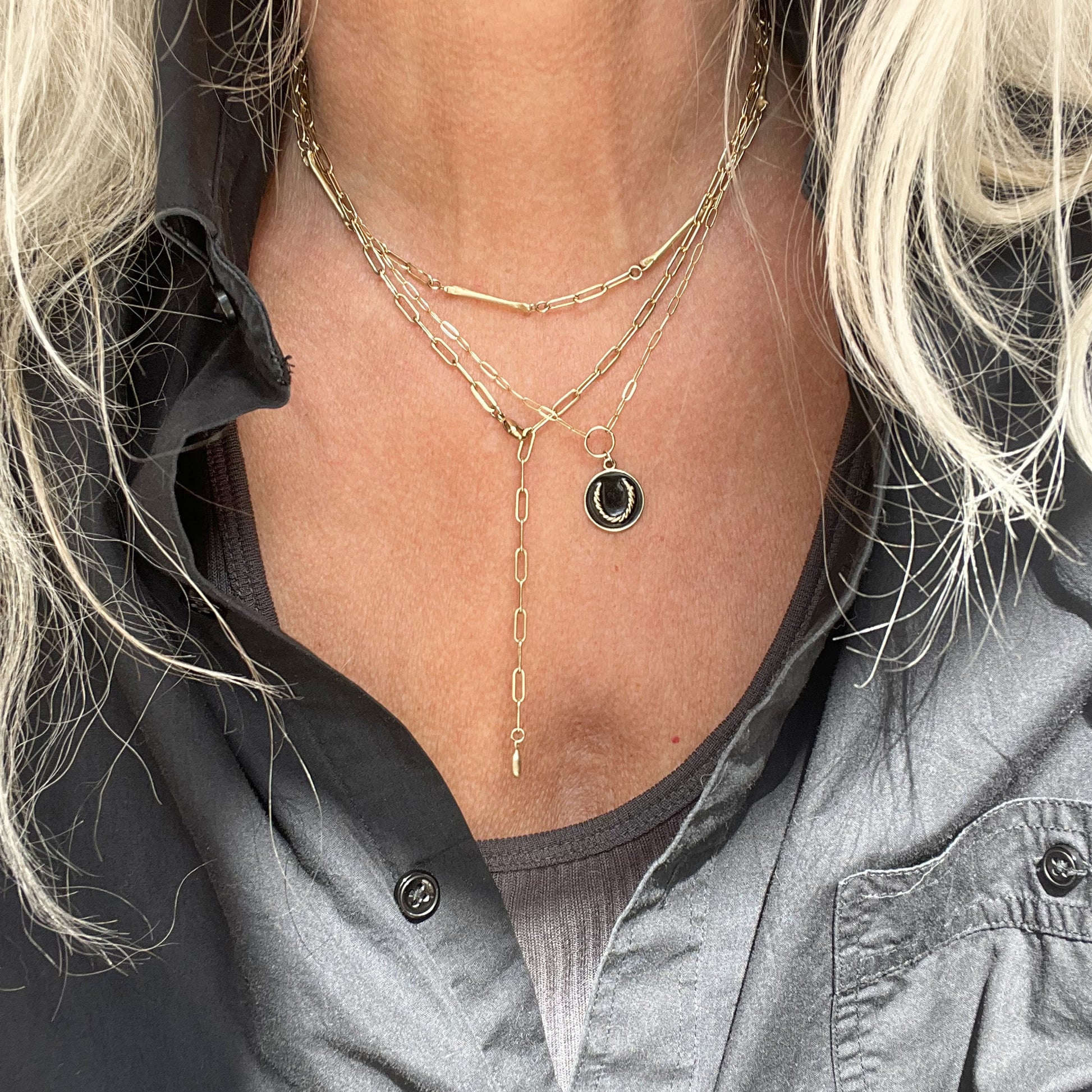 Gold-filled paperclip chain with eight evenly spaced solid reclaimed brass coyote paw bones 0.75 inches each and brass Kria tag adjustable 14 - 18 inches handmade and finished in our Catskills store-studio shown on model with Gold Roped Horseshoe Charm necklace.