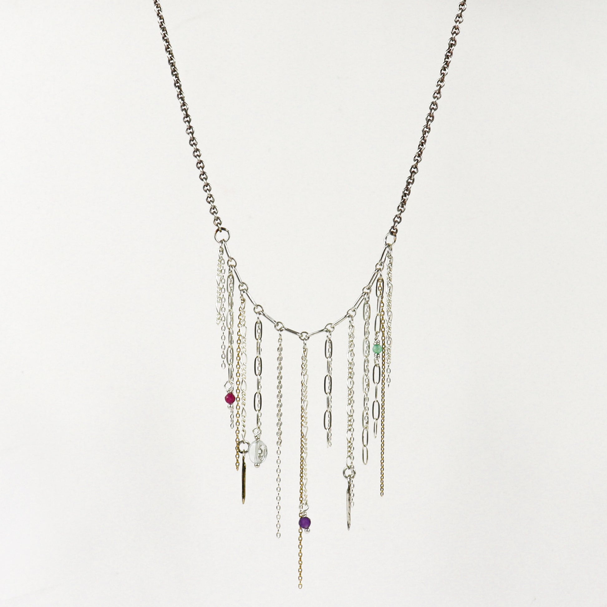 A silver-toned multi-strand fringe necklace handmade by Kria World with dangling chains, paperclip links, and small colorful beads on a plain white background.