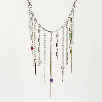 A silver-toned multi-strand fringe necklace handmade by Kria World with dangling chains, paperclip links, and small colorful beads on a plain white background.