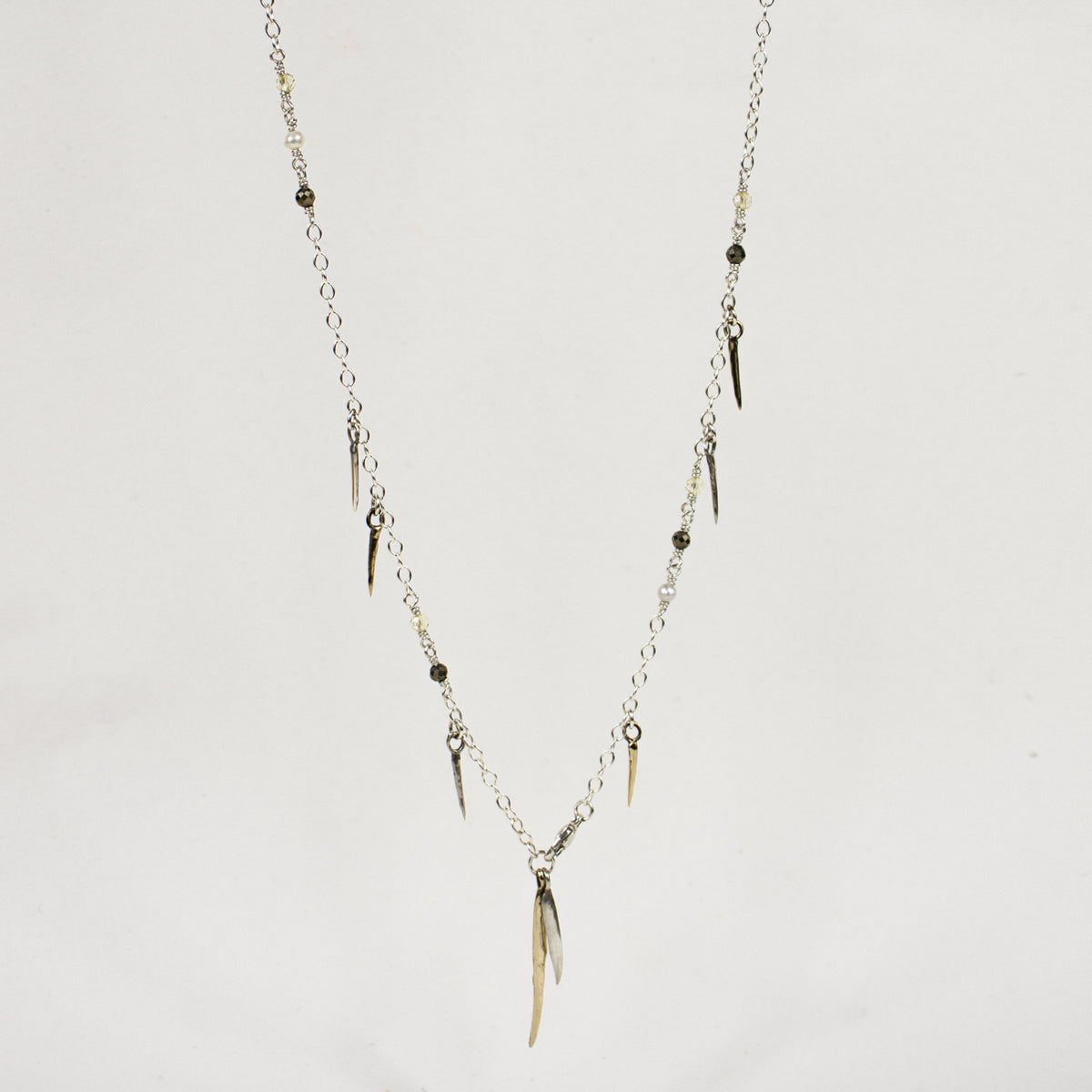 Sterling silver front clasp necklace beaded with pyrite, freshwater pearl, and brass and sterling silver spikes by Kria World shown on a white background.