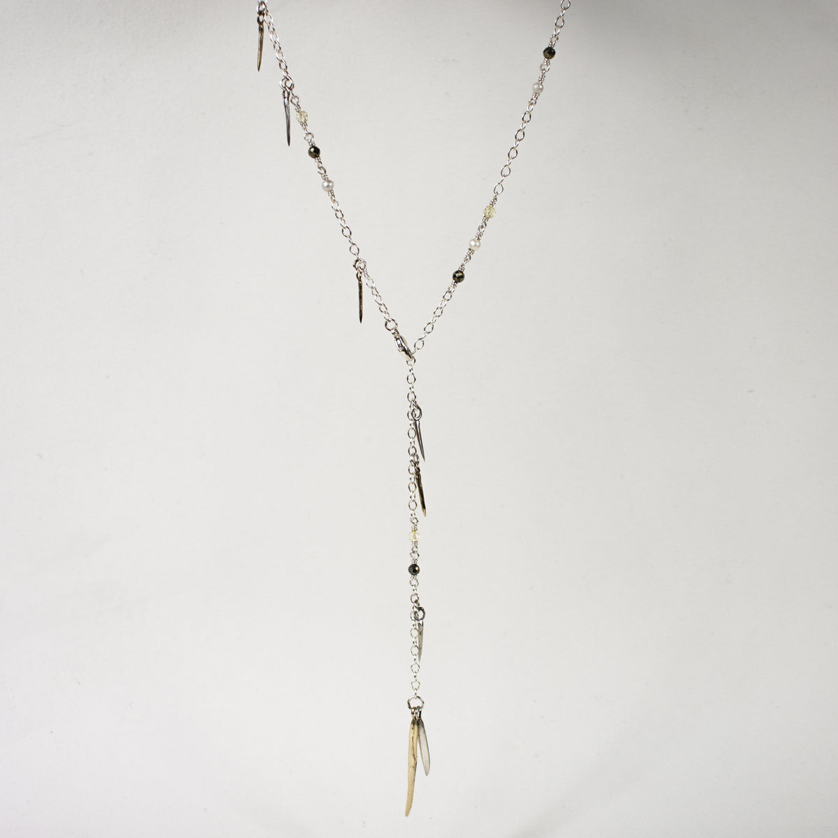 Sterling silver front clasp necklace beaded with pyrite, freshwater pearl, and brass and sterling silver spikes by Kria World shown on a white background.