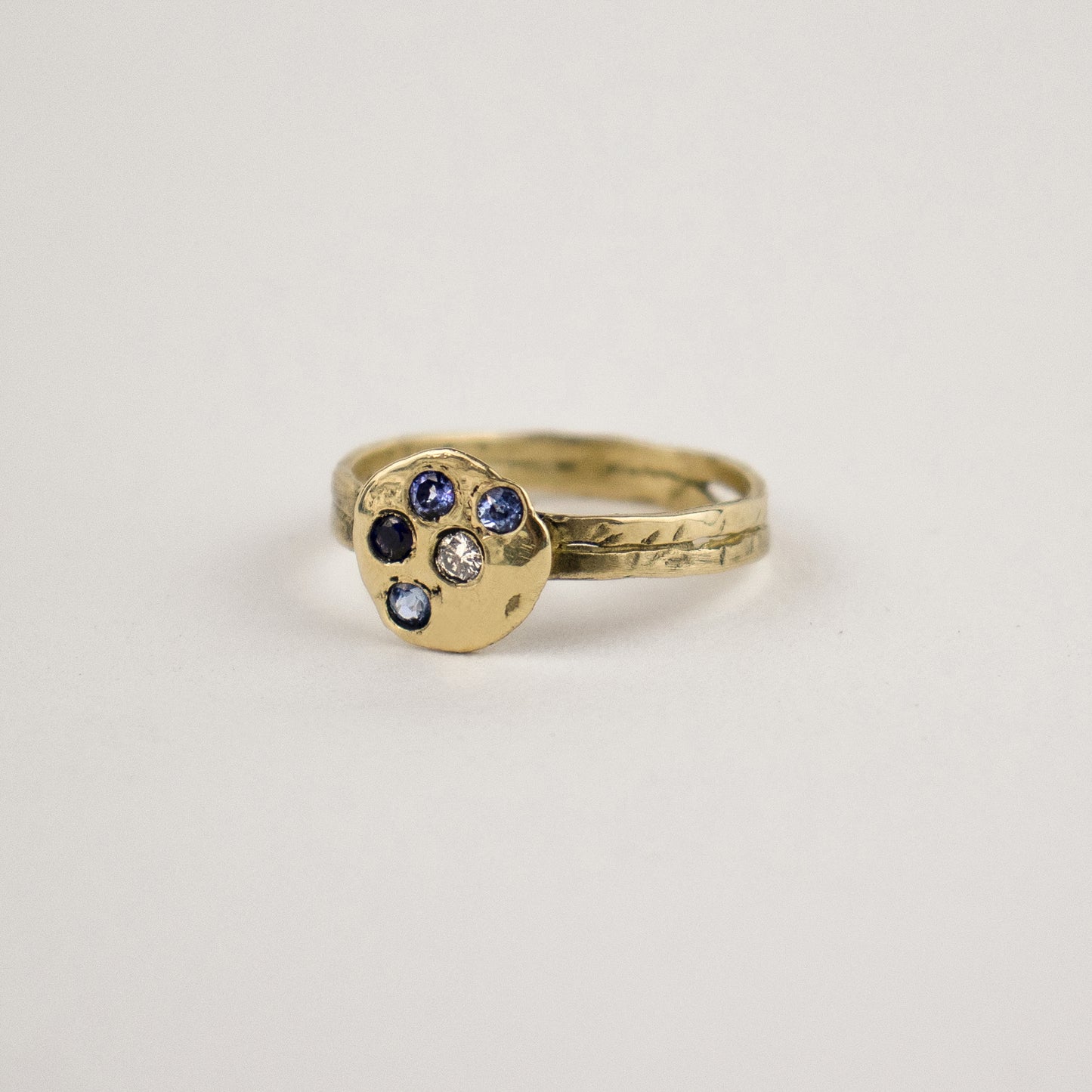 Solid reclaimed 14k gold hammer-finished Maine rock ring set with four 2 mm sapphires and one 2 mm diamond with ring face 0.5 inch in diameter. Handmade and finished in our Catskills store-studio.