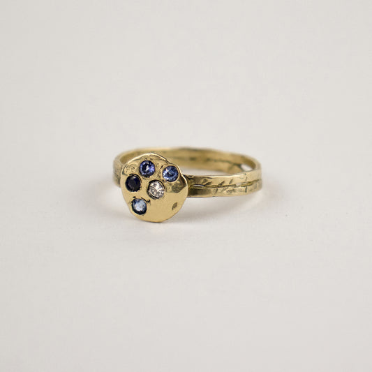 Solid reclaimed 14k gold hammer-finished Maine rock ring set with four 2 mm sapphires and one 2 mm diamond with ring face 0.5 inch in diameter. Handmade and finished in our Catskills store-studio.