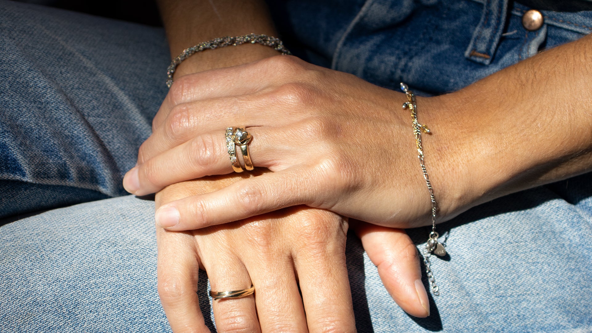 Closeup of model's hands in lap wearing a three Kria 14k gold rings set with diamonds with bracelets handmade with reclaimed gold and sterling silver and finished in our Catskills store-studio by NewYork-based Icelandic designer, Johanna Methusalemsdottir.