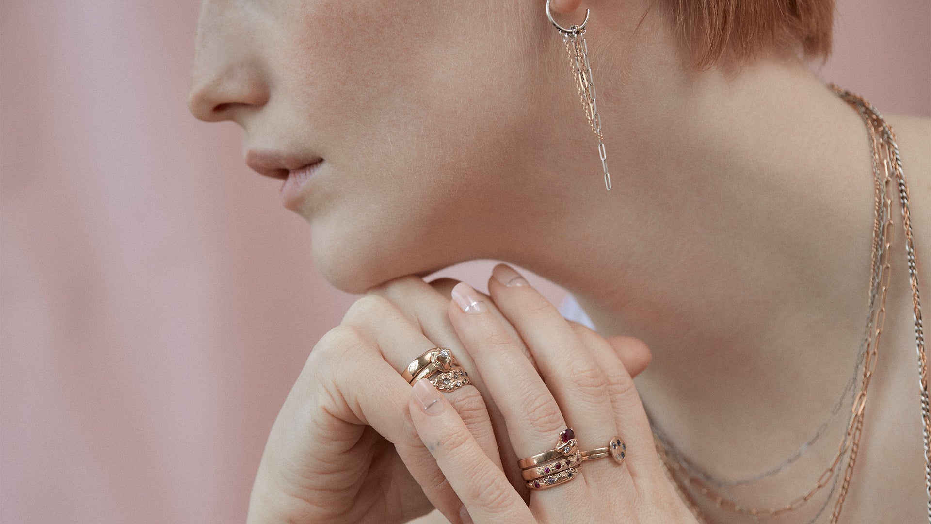 Closeup of model wearing several Kria 14k gold rings set with precious stones and mixed-chain necklaces and earrings all handmade with reclaimed metals and finished in our Catskills store-studio by NewYork-based Icelandic designer, Johanna Methusalemsdottir.