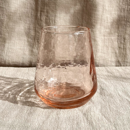 Hand-blown hammered glass tumblers in blush or smoke tints and measuring 4 inches in height and 3 inches in diameter at the base.