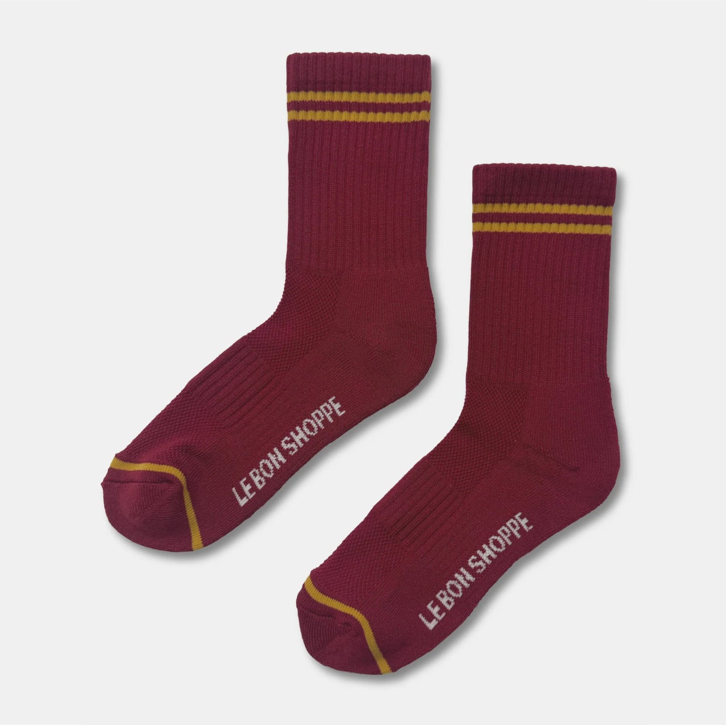 A pair of crew socks in cardinal with yellow stripes near the cuff and yellow toe trim, featuring the brand name 'LEBON SHOPPE' printed in white on the sole of each sock, set against a light gray background.