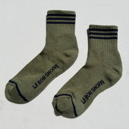 A pair of sage green crew socks with dark navy stripes on the cuff and navy branding text reading 'LE BON SHOPPE' on the sole, displayed on a light gray background.
